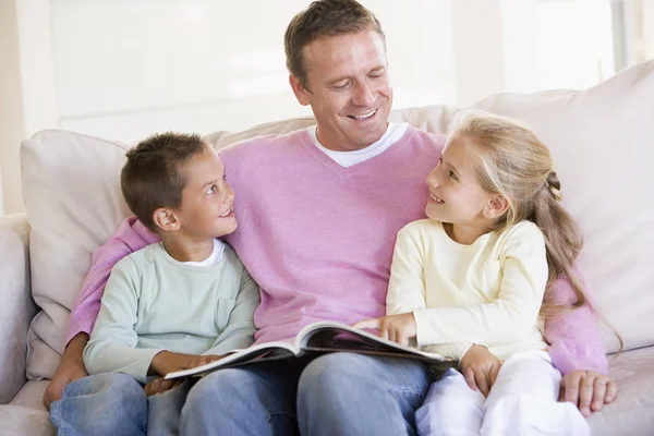 Man and two children sitting in living room reading book and smi — Stock Photo, Image