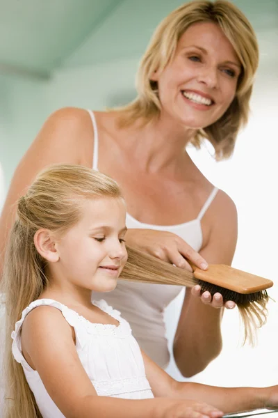 Femme dans la salle de bain brossant les cheveux de la jeune fille — Photo