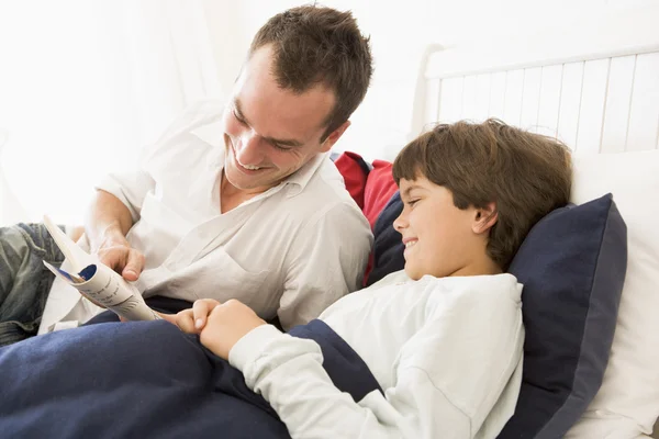 Man reading book to young boy in bed smiling — Stock Photo, Image
