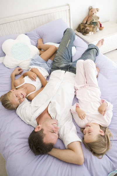 男子躺在床上和两个年轻女孩微笑 — 图库照片