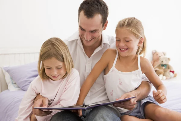 Hombre en el dormitorio con dos chicas jóvenes leyendo libro y sonriendo —  Fotos de Stock