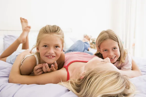 Γυναίκα ξαπλωμένη στο κρεβάτι με δύο νεαρά κορίτσια που χαμογελά — Φωτογραφία Αρχείου