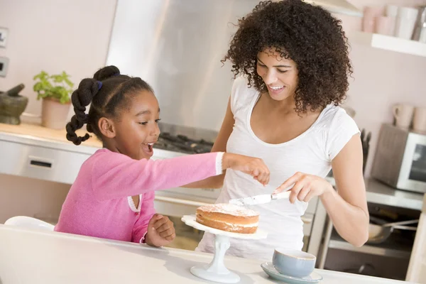 笑みを浮かべて、ケーキのアイシングの台所で女性および若い女の子 — ストック写真