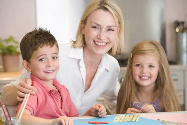 Vrouw en twee kinderen in keuken met kunst project lachende — Stockfoto