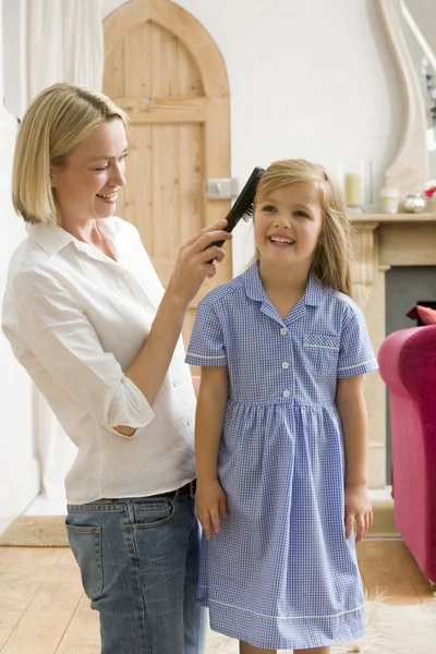 Woman in front hallway brushing young girl's hair and smiling — Stock Photo, Image
