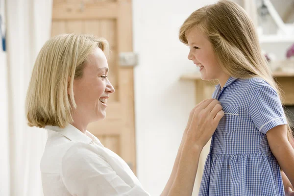 Woman in front hallway fixing young girl's dress and smiling — Stock Photo, Image