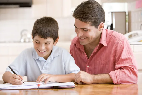 Uomo aiutare giovane ragazzo in cucina facendo i compiti e sorridendo — Foto Stock