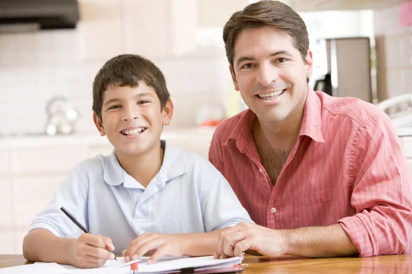 Muž pomáhá mladý chlapec v kuchyni dělat domácí úkoly a s úsměvem — Stock fotografie