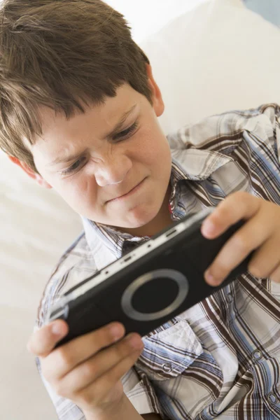 Мальчик с ручной игрой в помещении выглядит несчастным — стоковое фото