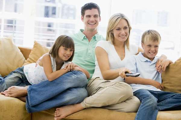Familjen sitter i vardagsrummet med fjärrkontroll leende — Stockfoto