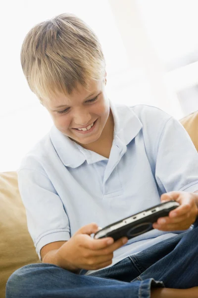 Мальчик в гостиной с улыбкой на ручной видеоигре — стоковое фото