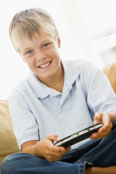 Мальчик в гостиной с улыбкой на ручной видеоигре — стоковое фото