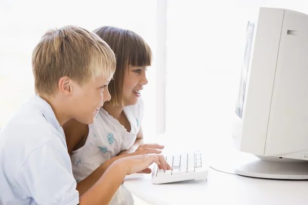 Двое маленьких детей в домашнем офисе с улыбкой на компьютере — стоковое фото