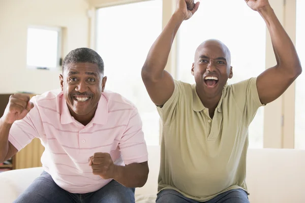 Two men in living room cheering and smiling — Stock Photo, Image