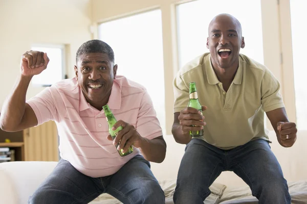 Δύο άνδρες στο σαλόνι με μπουκάλια μπύρας, επευφημίες και χαμογελαστός — Φωτογραφία Αρχείου