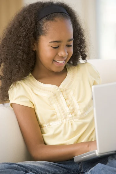 Chica joven en la sala de estar utilizando el ordenador portátil y sonriendo — Foto de Stock