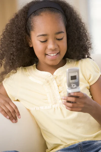 Ung flicka i vardagsrummet med hjälp av mobiltelefon och ler — Stockfoto