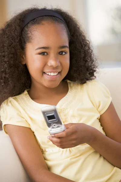 Νεαρό κορίτσι στο σαλόνι, χρήση κινητού τηλεφώνου και χαμογελαστός — Φωτογραφία Αρχείου
