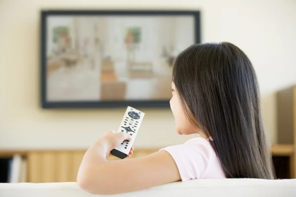 Молодая девушка в гостиной с телевизором с плоским экраном и пультом — стоковое фото