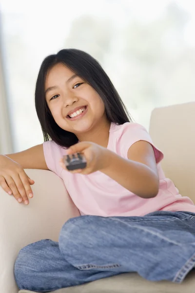 Young girl in living room with remote control smiling — Stock Photo, Image
