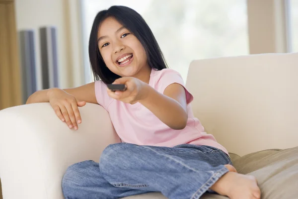 Mladá dívka v obývacím pokoji s úsměvem a dálkové ovládání — Stock fotografie