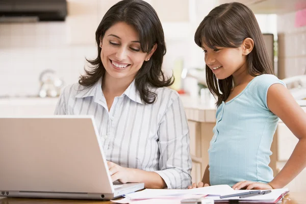 Mulher e menina na cozinha com laptop e papelada sorridente — Fotografia de Stock