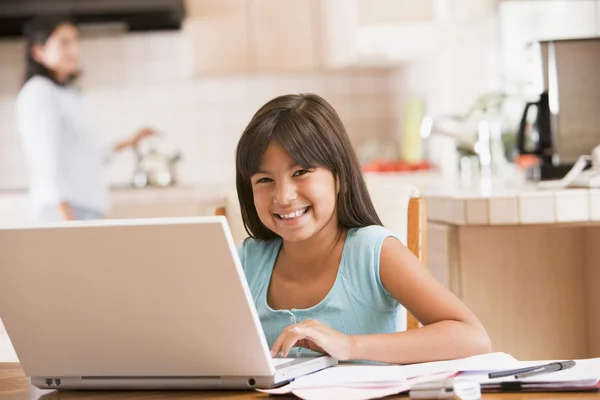 Junges Mädchen in der Küche mit Laptop und Papierkram lächelnd mit wom — Stockfoto