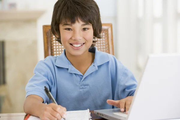 Ung pojke med laptop gör läxor i matsal leende — Stockfoto