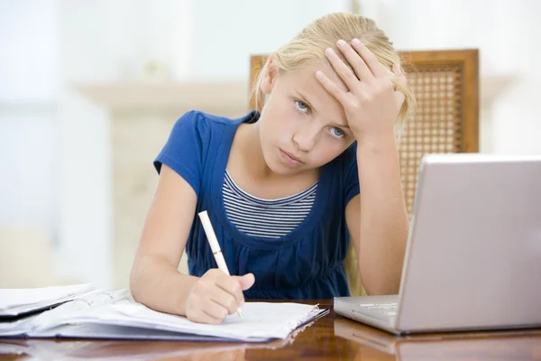 Chica joven con el ordenador portátil haciendo la tarea en el comedor mirando unh —  Fotos de Stock