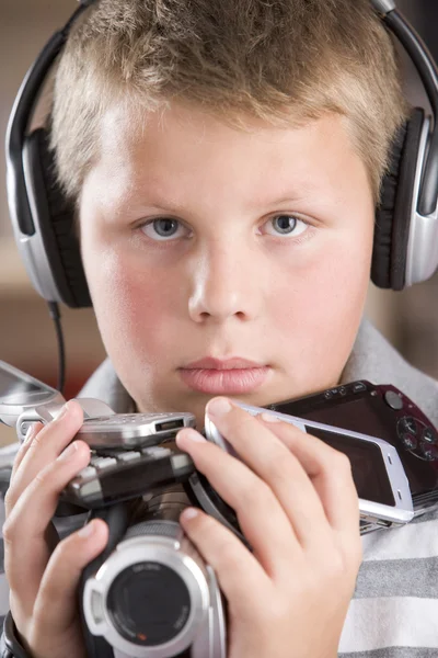 Młody chłopak sobie słuchawki w sypialni, posiadający wiele elektronicznych — Zdjęcie stockowe