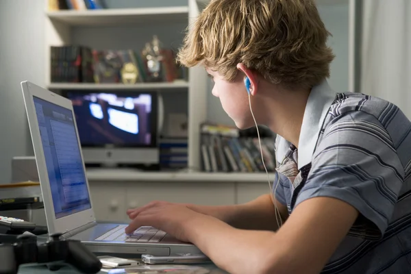Young boy in bedroom using laptop and listening to MP3 player — Stock Photo, Image
