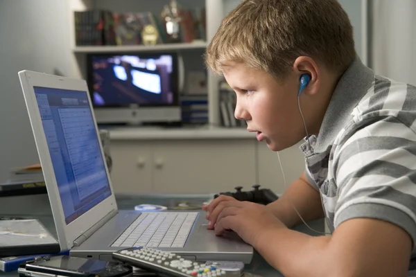 小男孩在卧室使用的便携式计算机和听 mp3 播放器 — 图库照片