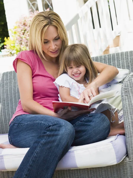 Mujer y niña sentada en el patio leyendo libro sonriendo —  Fotos de Stock