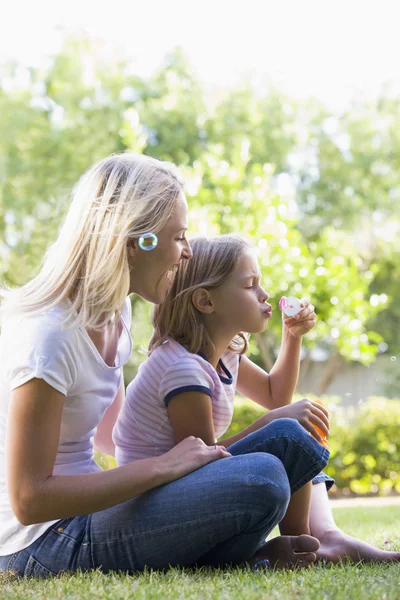 Vrouw en jonge meisje buiten blazen luchtbellen glimlachen — Stockfoto