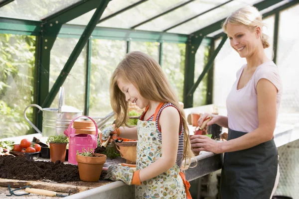Ung flicka och kvinna i växthus att sätta jord i krukor leende — Stockfoto