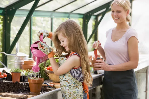 Chica joven en planta de riego de invernadero con mujer sosteniendo la olla s — Foto de Stock
