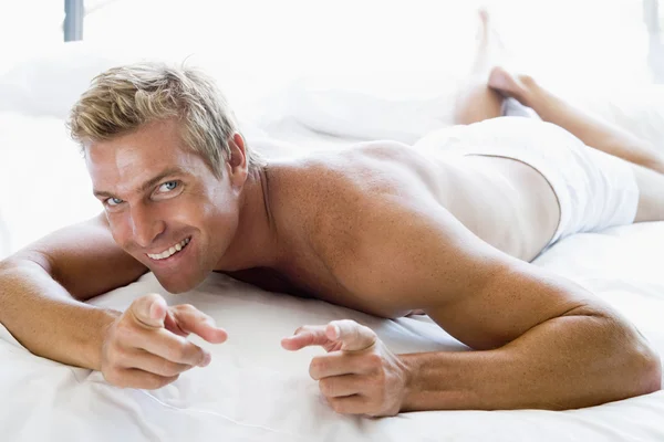 指していると笑みを浮かべてベッドに横たわっている男 — ストック写真