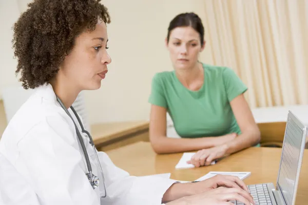 Doctor using laptop with woman in doctor's office frowning — Stock Photo, Image
