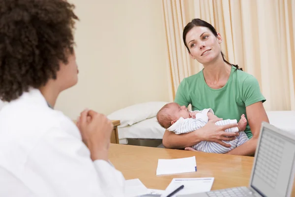 Arzt mit Laptop und Frau in Arztpraxis mit Baby — Stockfoto