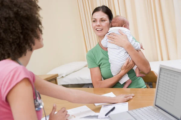 Doutor com laptop e mulher no escritório do médico segurando bebê — Fotografia de Stock