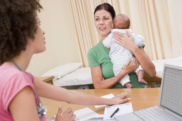 Arzt mit Laptop und Frau in Arztpraxis mit Baby — Stockfoto
