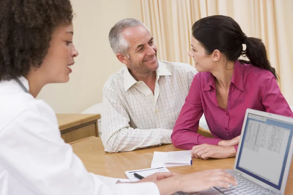 Läkare med laptop och par i läkarmottagningen leende — Stockfoto