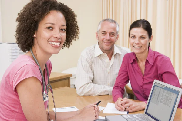 Arts met een laptop en paar in spreekkamer glimlachen — Stockfoto