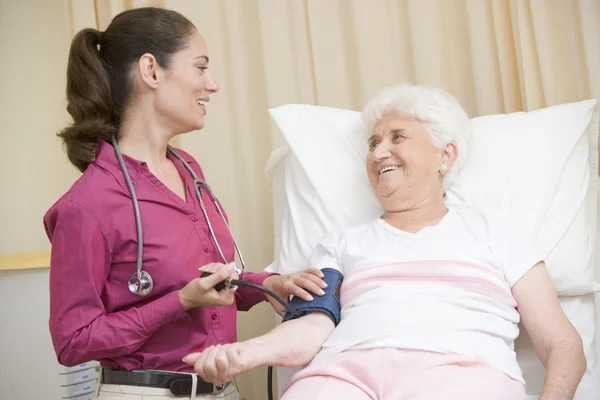 Лікар перевіряє кров'яний тиск жінки в аудиторії, посміхаючись — стокове фото