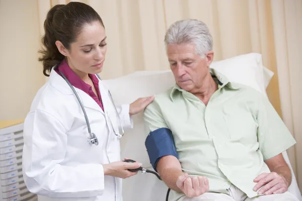 Médico revisando la presión arterial del hombre en la sala de examen —  Fotos de Stock