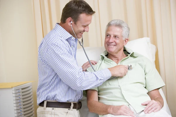 Lekarz daje sprawdzanie człowiek z stetoskop w egzamin pokój uśmiechający się — Zdjęcie stockowe