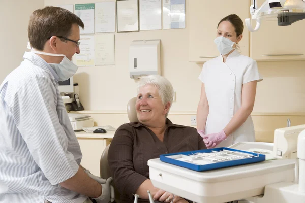 Dentista e assistente in sala esami con donna in sedia sorridente — Foto Stock