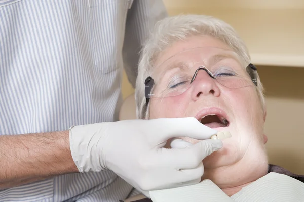 Dentist in exam room fitting dentures on woman in chair — Stock Photo, Image