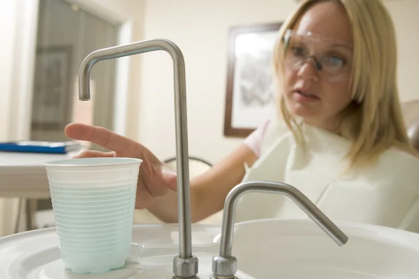 Женщина в стоматологической комнате тянется за водой — стоковое фото