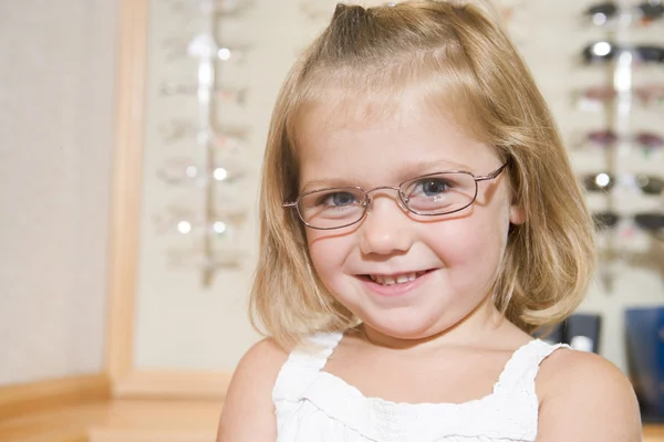 Молода дівчина приміряє окуляри в окулярах, посміхаючись — стокове фото